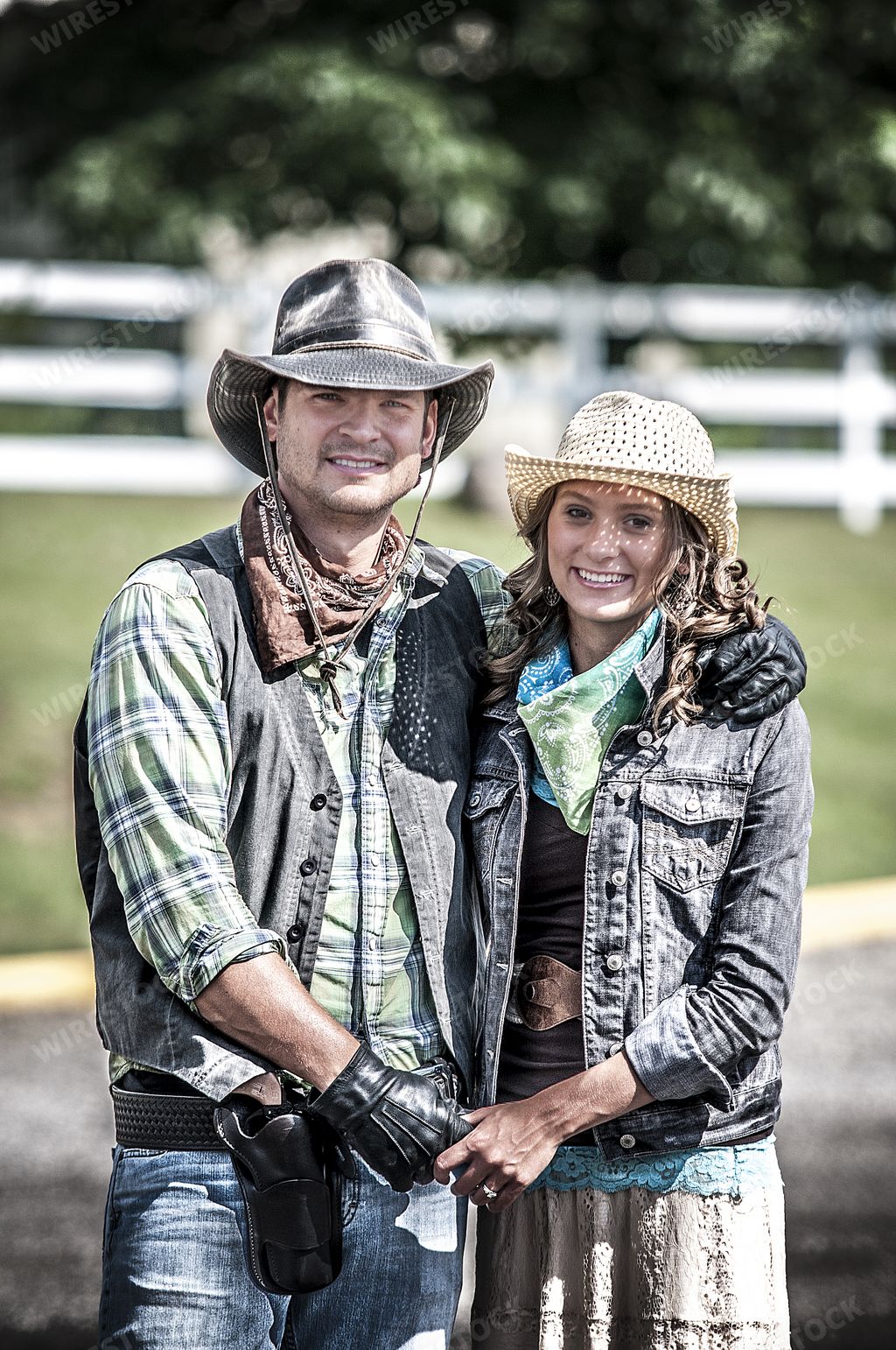 A vertical shot of a couple wearing a cowboy outfit holding hand while smiling at the camera