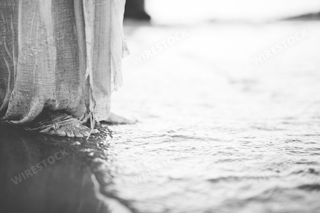 A closeup shot of a person wearing a biblical robe while standing on the shore in black and white