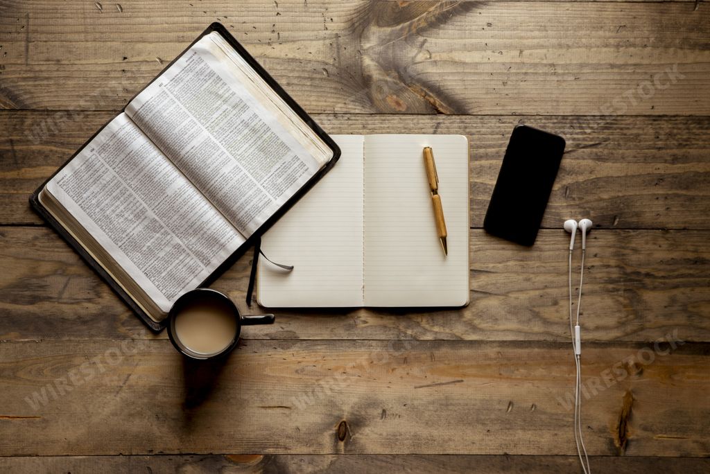 An overhead shot of a notebook with a fountain pen near an open book and smartphone on a wooden table