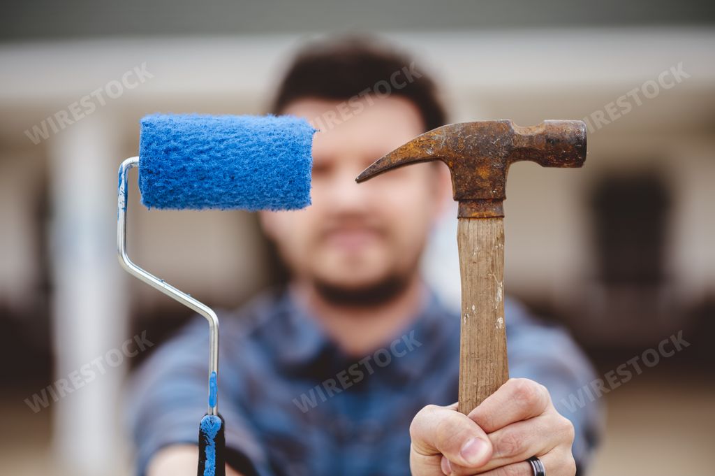 A soft focus of a man holding a paint roller with blue paint and an old rusty hammer