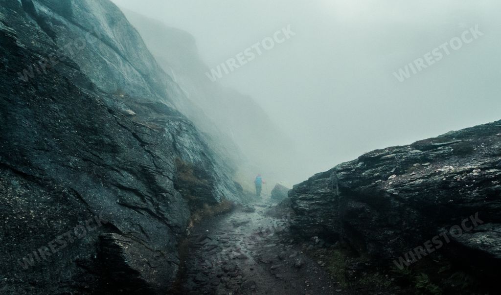 A wide shot of a narrow muddy pathway in the middle of cliffs covered with fog