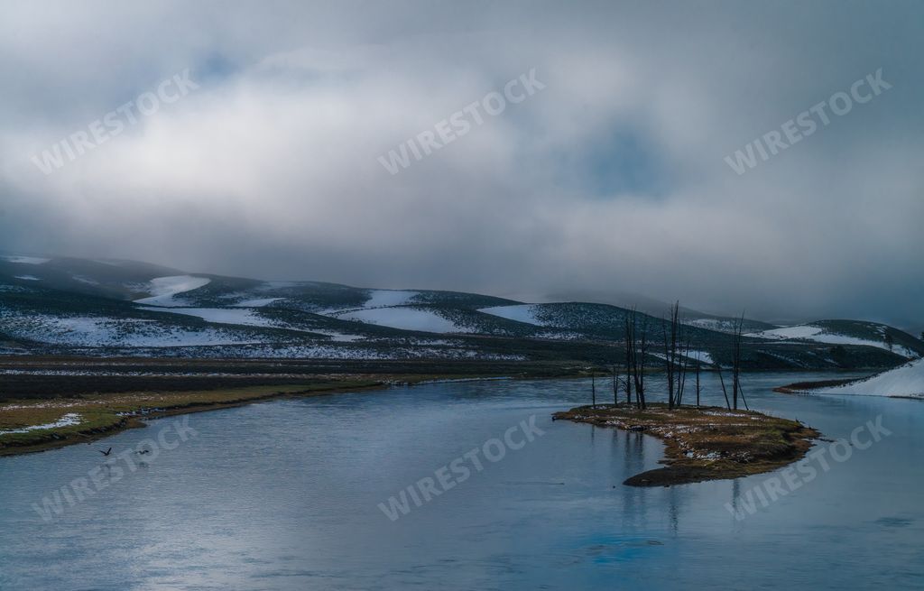 A beautiful scenery of a river surrounded by snowy hills on a cloudy day