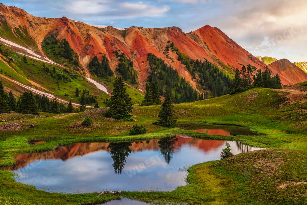 Scenic pond in lush field with mountains and cloudy sky
