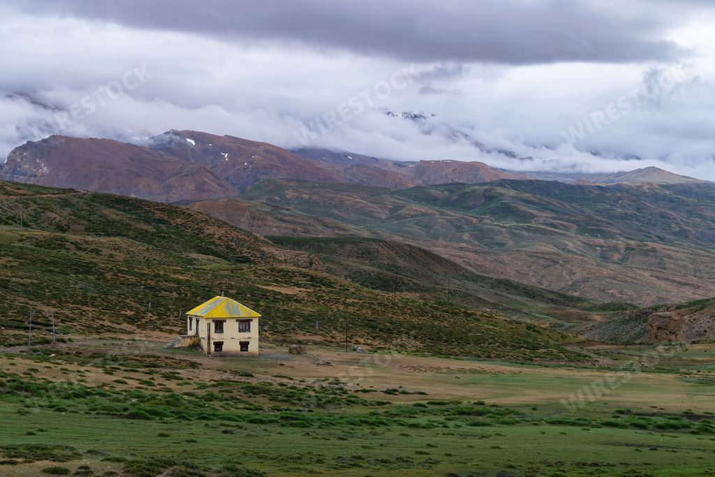 A lone house close to Tashigang village, India surrounded by mountains covered with clouds