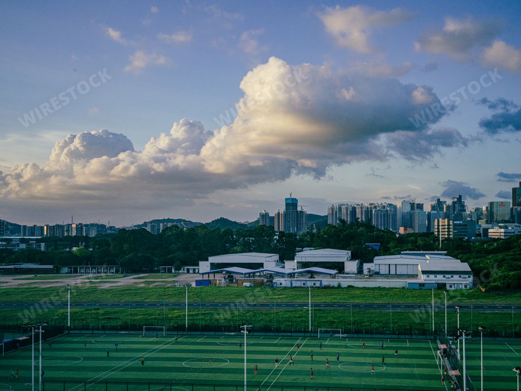 A beautiful view of football field with a big city in background and puffy clouds in the sky at sunset