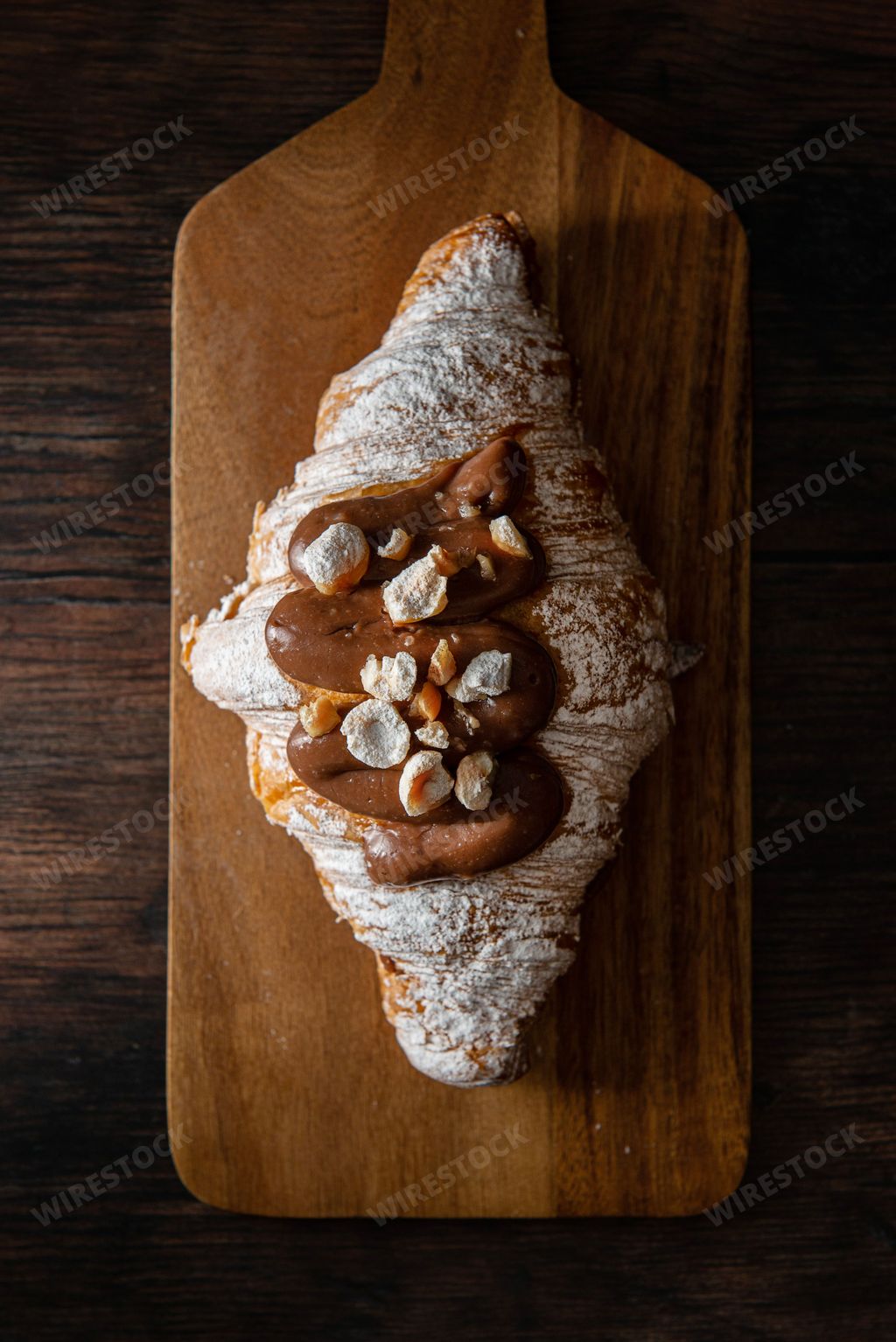 A vertical top view of a gourmet croissant with powdered sugar and chocolate cream on a wooden board