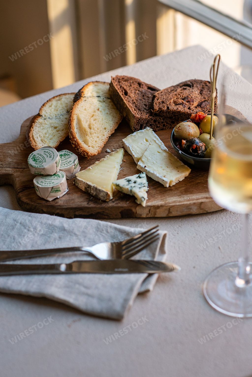A vertical shot of different kinds of cheese and bread on a wooden tray