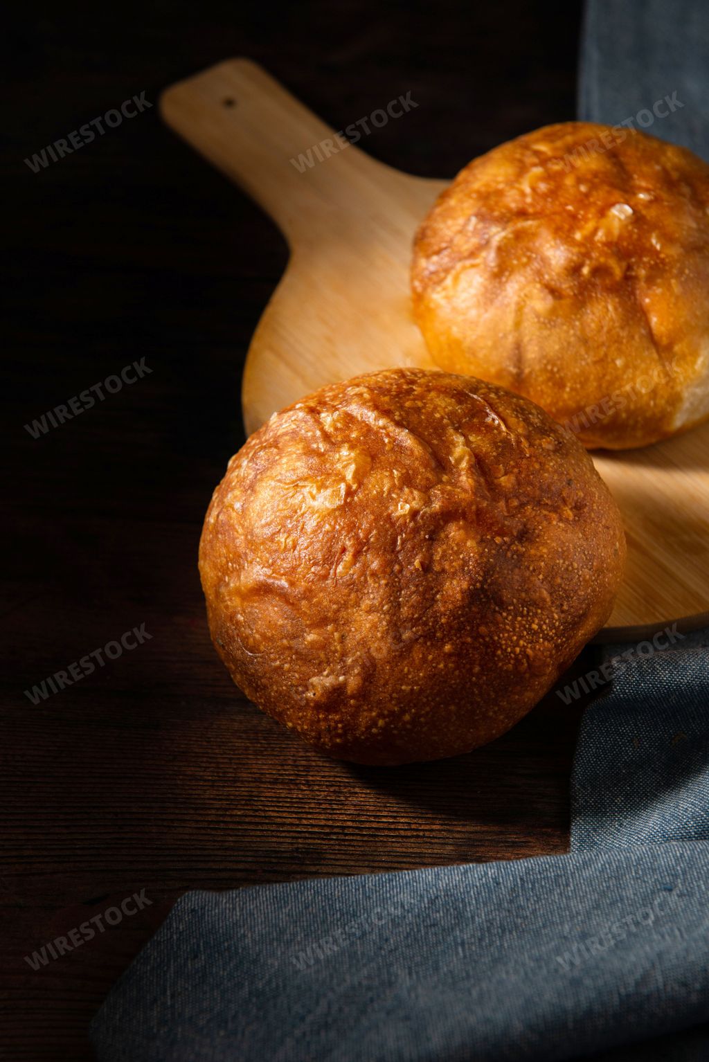 A vertical shot of a pair of sourdough bread on a circular wooden board