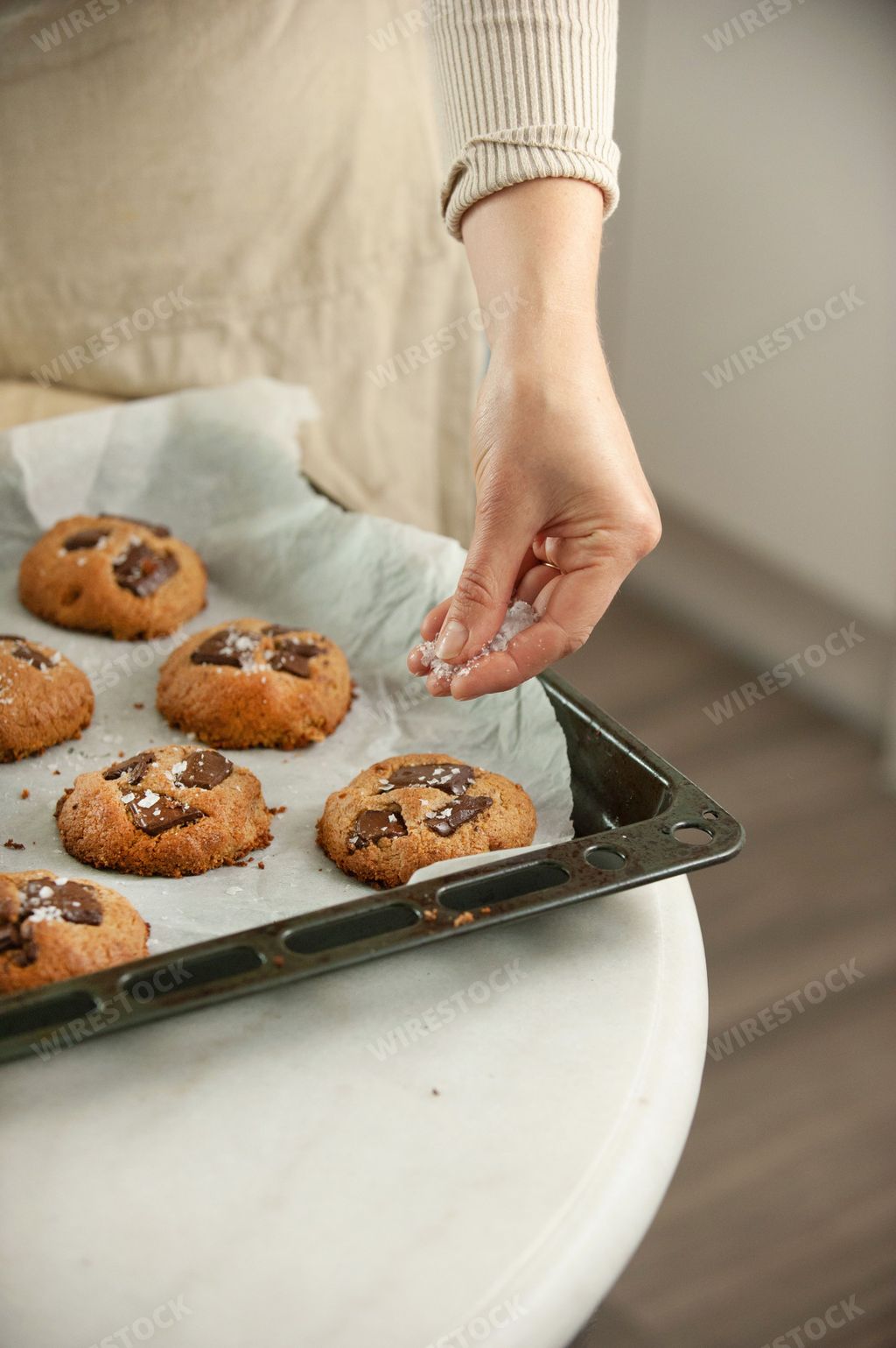 A vertical closeup of female hands putting cookies on the black baking sheet pouring on them other ingredients around