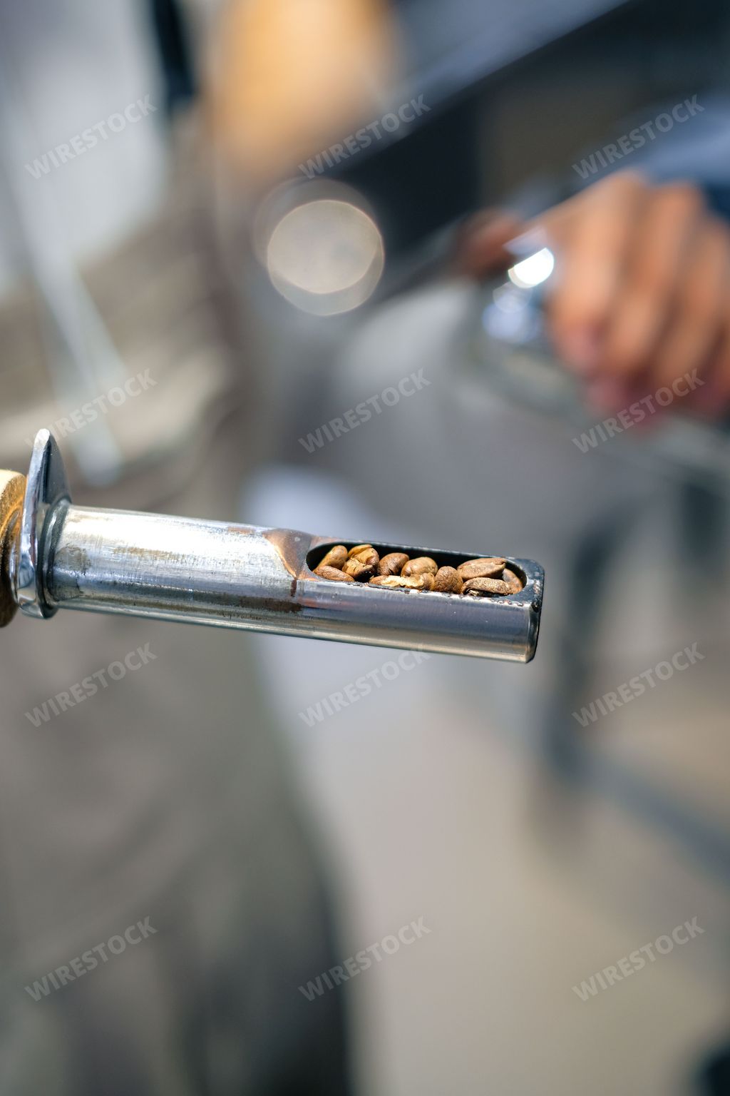 A vertical shot of a hand holding a thin coffee roaster with beans inside