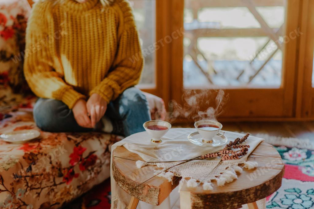 A beautiful shot of a girl sitting on a sofa and two cups of tea on a wooden table