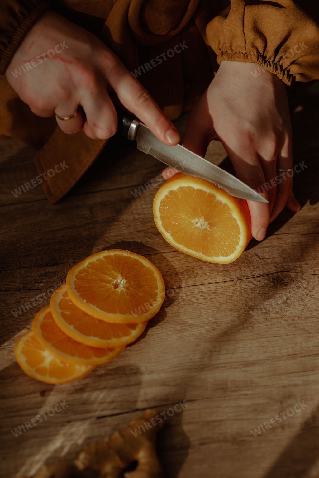 A vertical shot of a person cutting an orange on a cutting board
