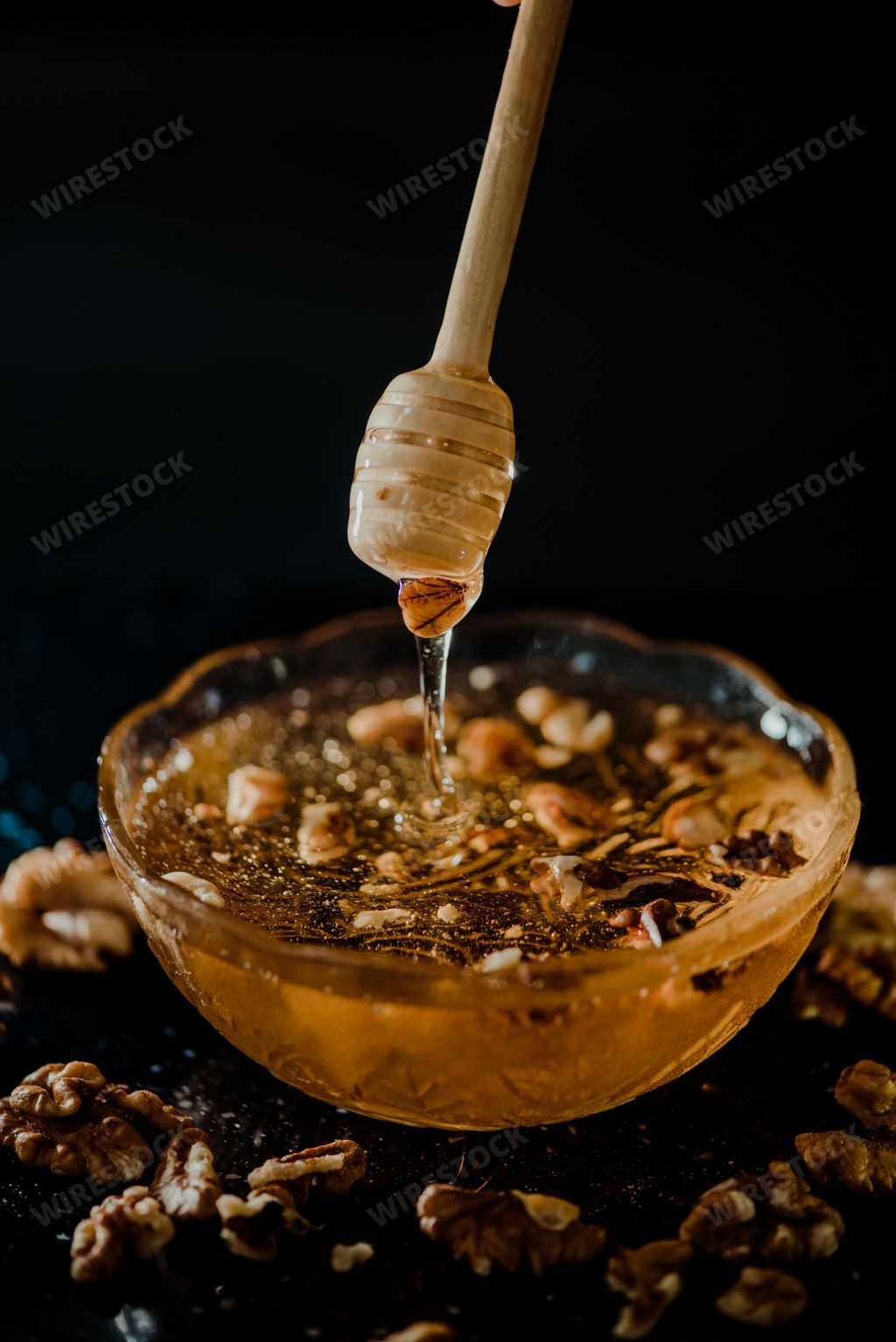 Wooden honey spoon dipped in a jar full of honey and nuts placed on a black background. Honey dripping around, pleasing and inviting photos.