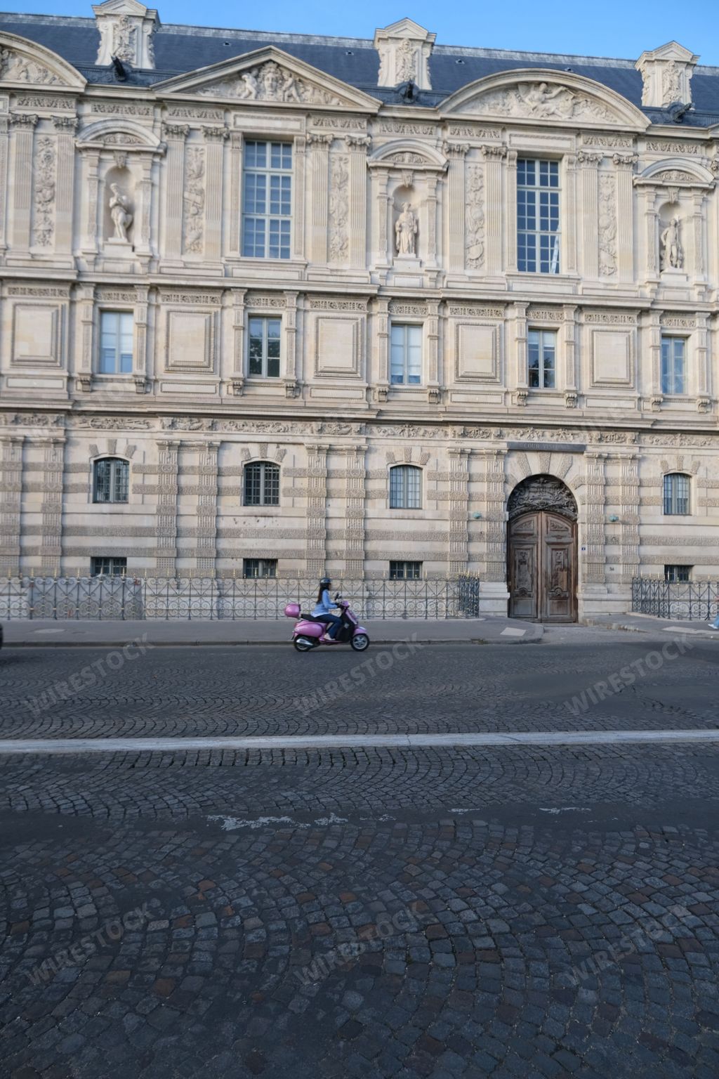 A vertical shot of a motorcyclist passing by a side door of the Louvre in Paris, France