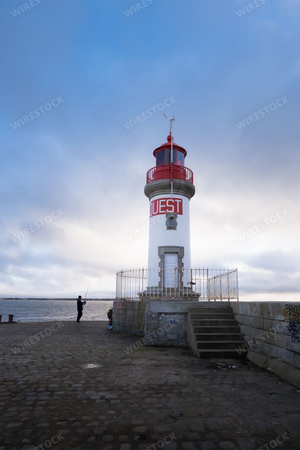 A fisherman standing near a lighthouse on the pier. Saint Nazaire