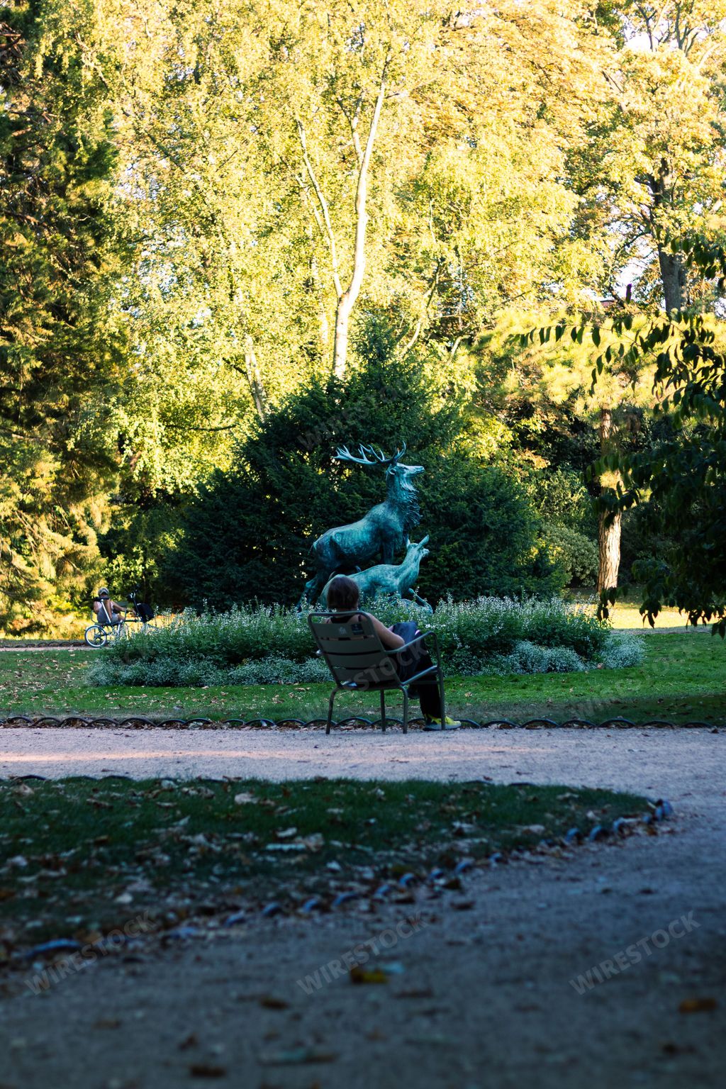 The vertical shot of a woman sitting in front of the statue of Harde de Cerf in Luxembourg Garden, Paris