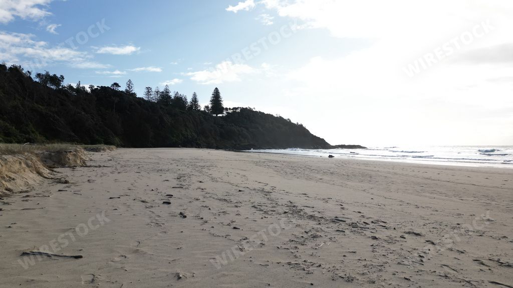 An empty beach with few ocean waves under a cloudy afternoon sky