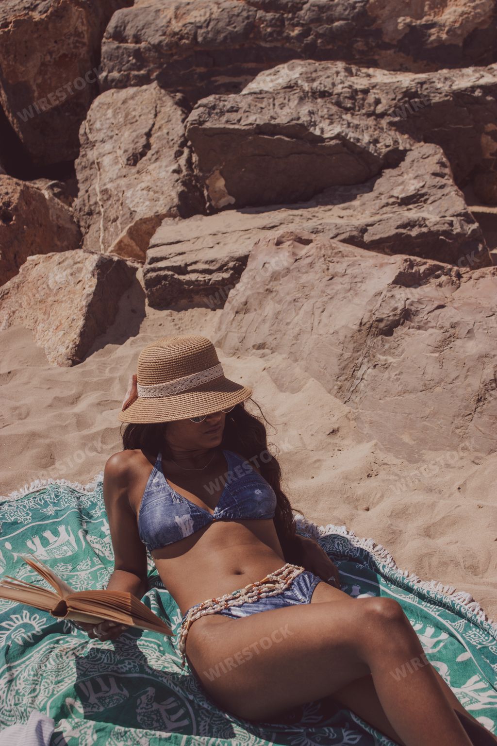 A sexy female lying on the sand near the rocks and reading her book and enjoying a sunny day