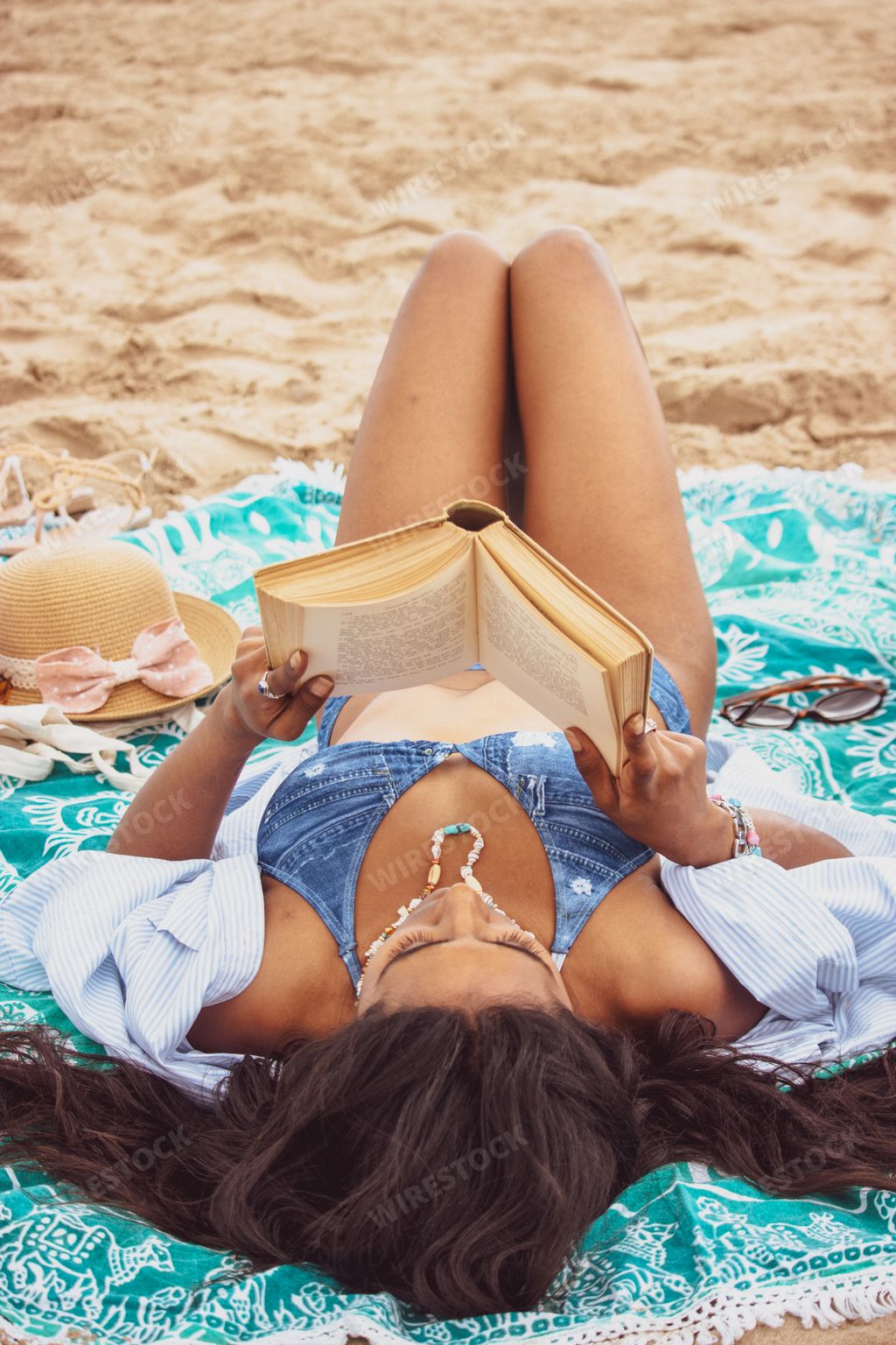 A young female lying on the sandy beach and reading a book