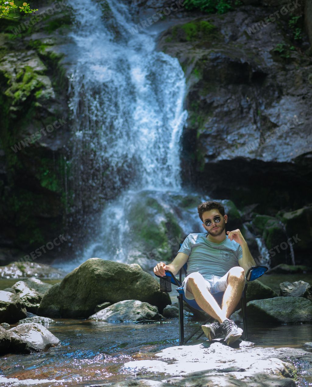 A vertical shot of a male sitting on a chair on the background of a waterfall in Yalova, Turkey