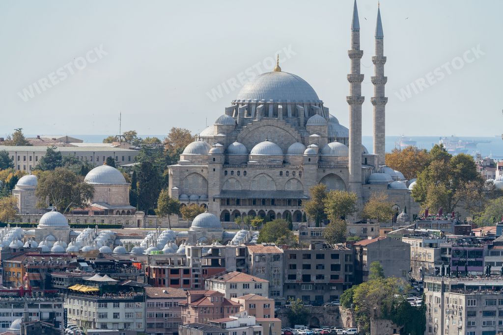 An aerial view of a large silver dome mosque with numerous windows, situated against a stunning city skyline