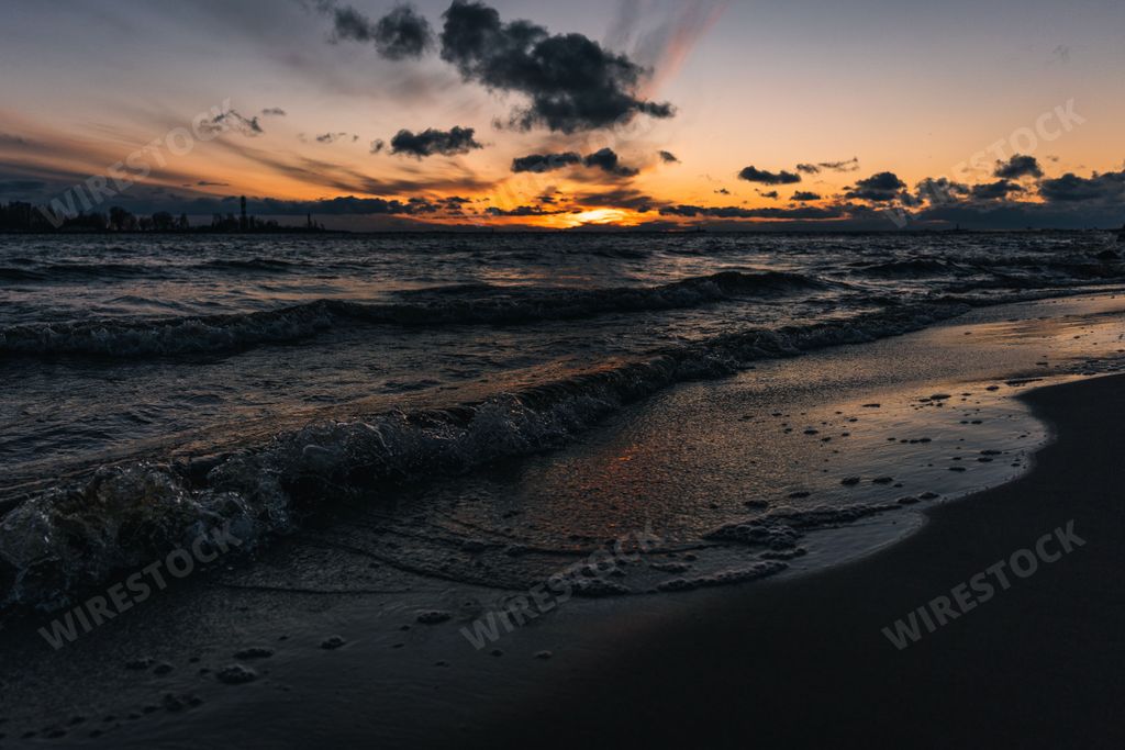A scenic view of ocean waves crashing against the beach at a cloudy sunset