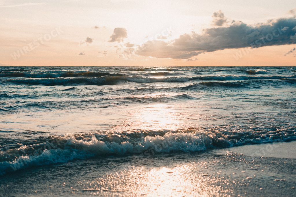 A scenic view of ocean waves crashing against the beach at a cloudy sunset