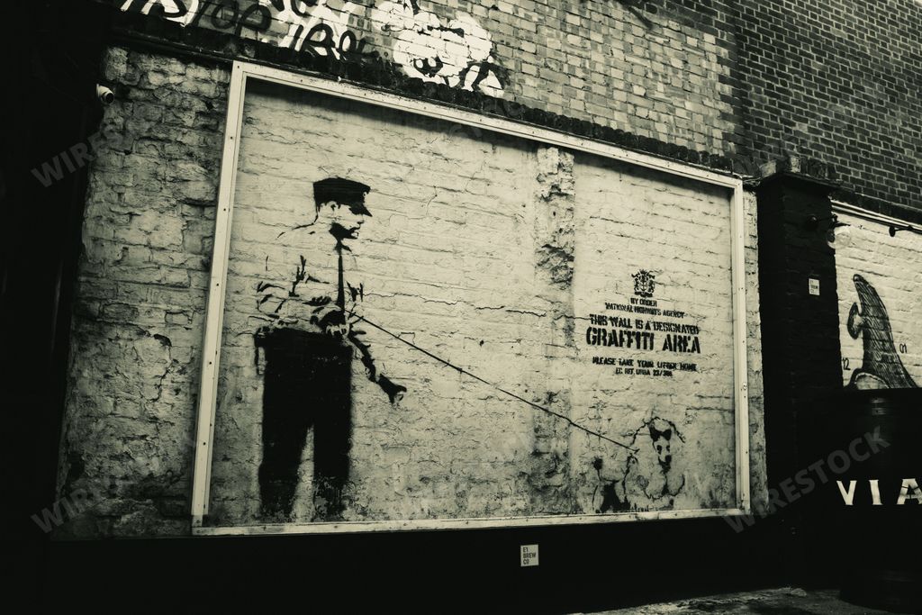 A grayscale shot of street art by Banksy on a designated graffiti wall in London, England