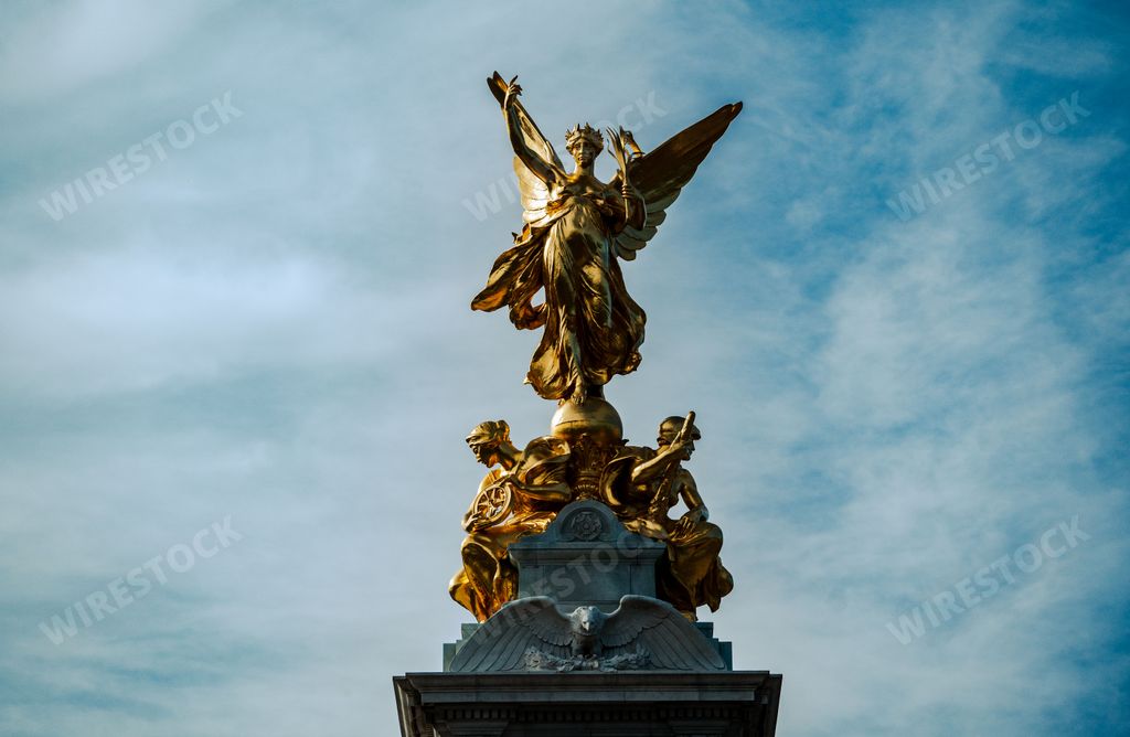 A gleaming golden statue stands illuminated in the evening light in front of the grand facade of Buckingham Palace in London, England