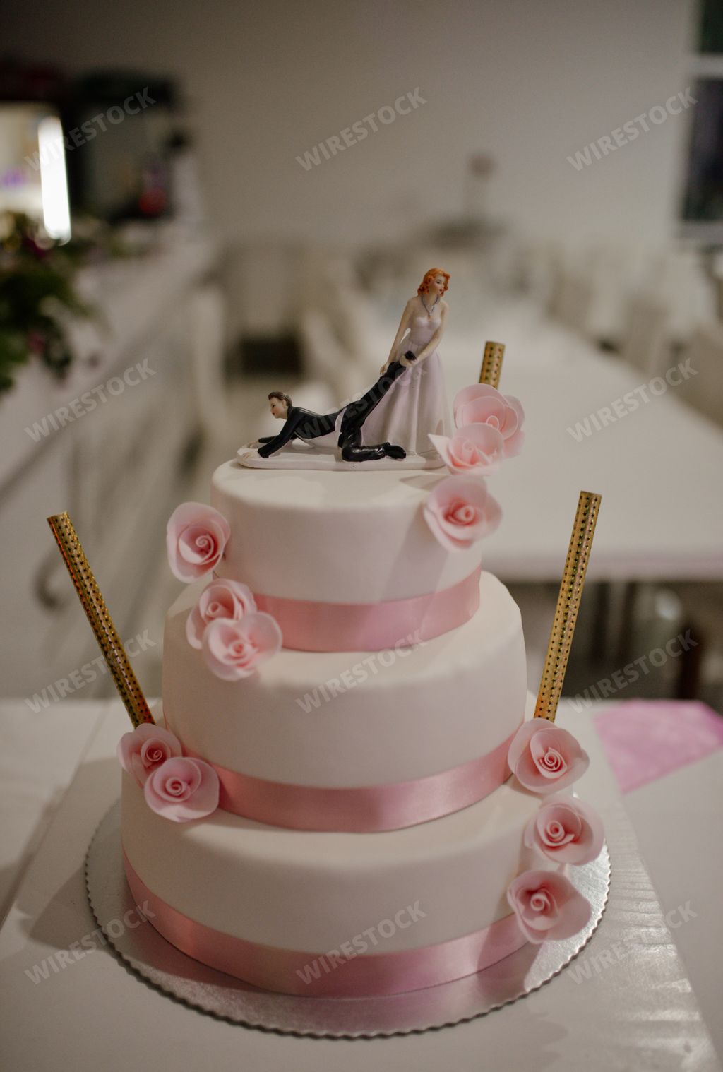A selective focus shot of funny figurines on the top of a white wedding cake decorated with pink flowers and ribbons