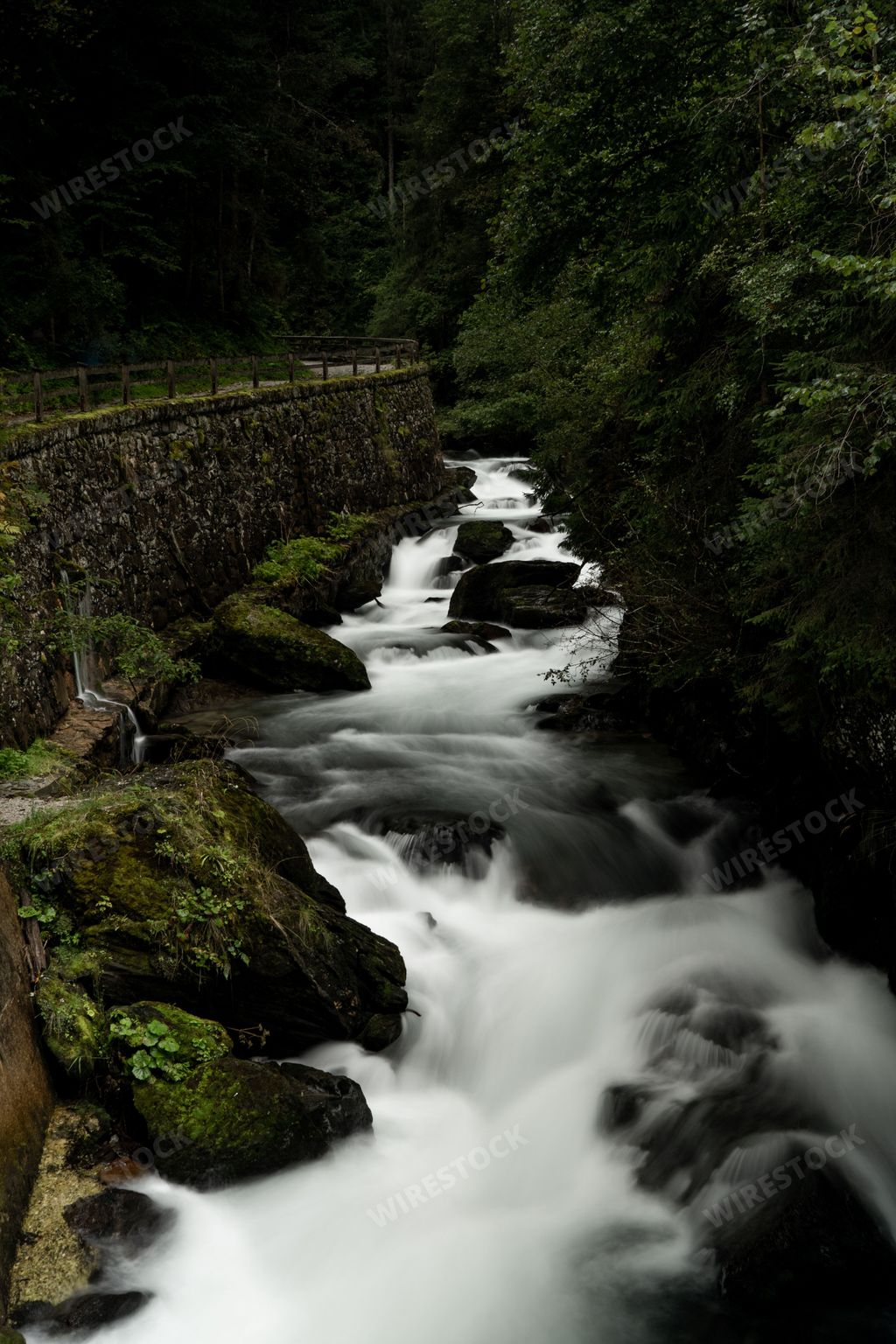 A vertical long exposure of a waterfall stream surrounded by rocks covered in moss