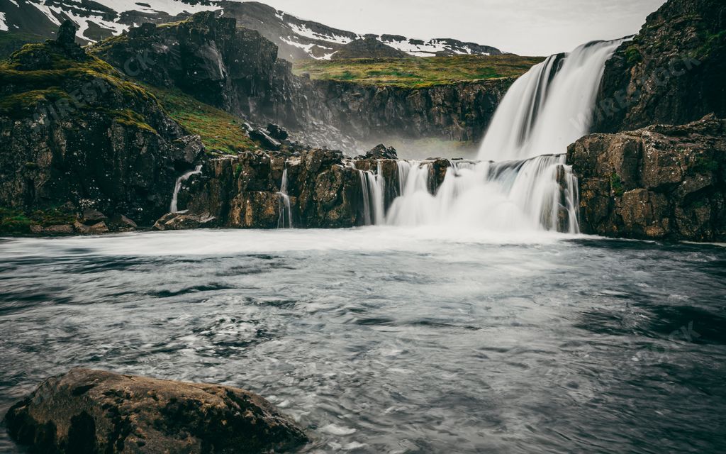 A majestic waterfall cascading from a lush valley near the mountains in Seydisfjordur, Iceland