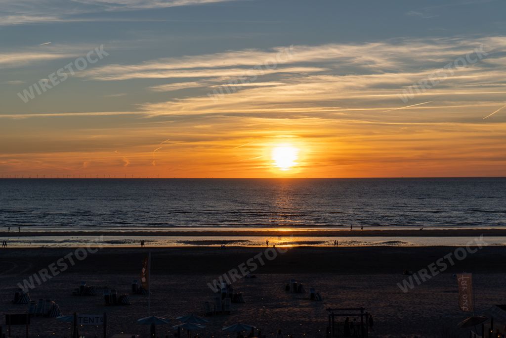 A bright golden sunset over the calm blue sea and the sandy beach with the horizon in the background
