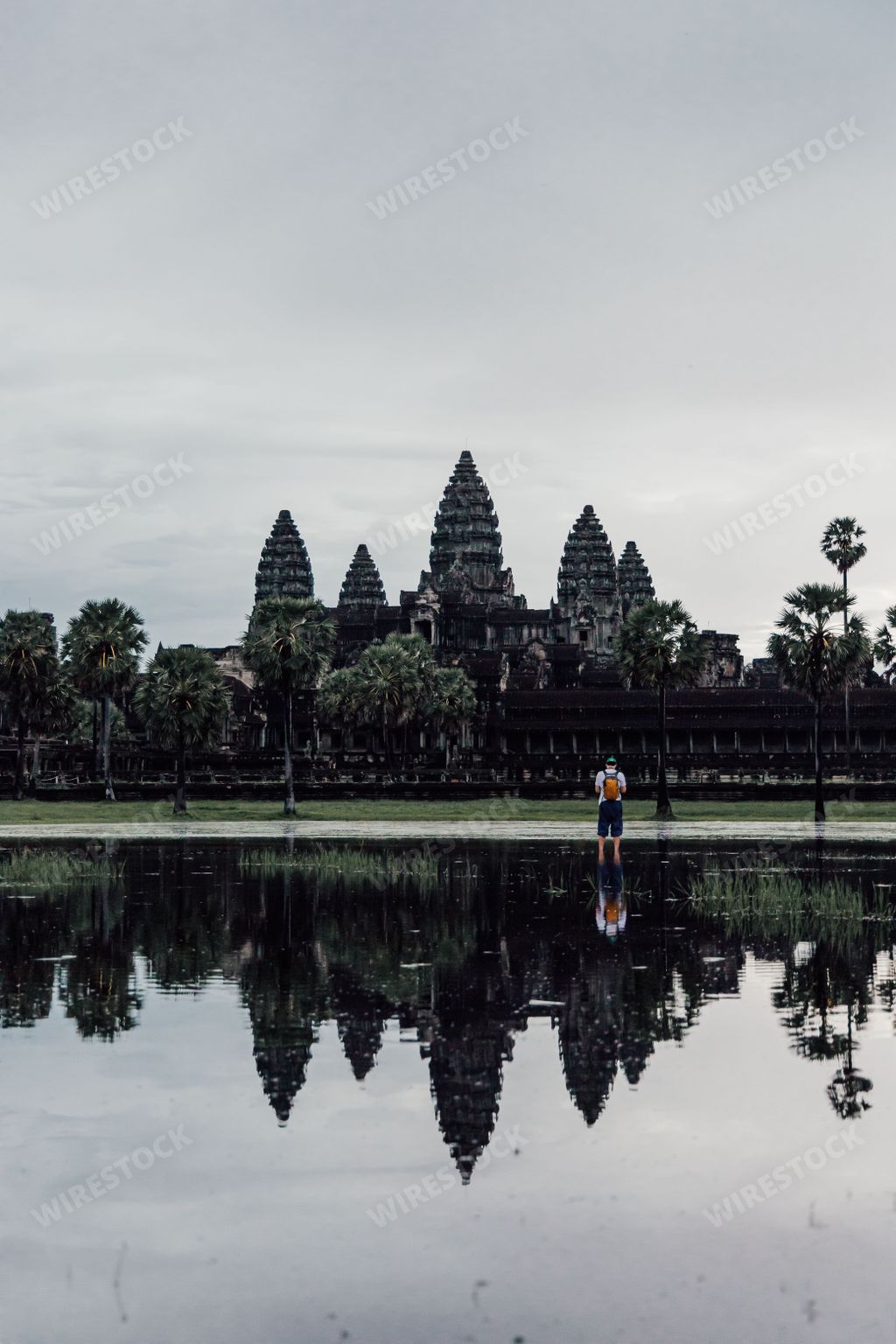 A vertical shot of a tourist in front of Angkor Wat Buddhist temple in Cambodia