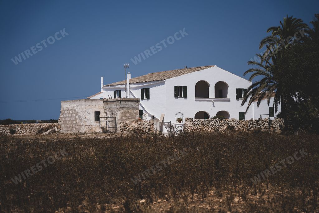 An old white house with arched doors in the field