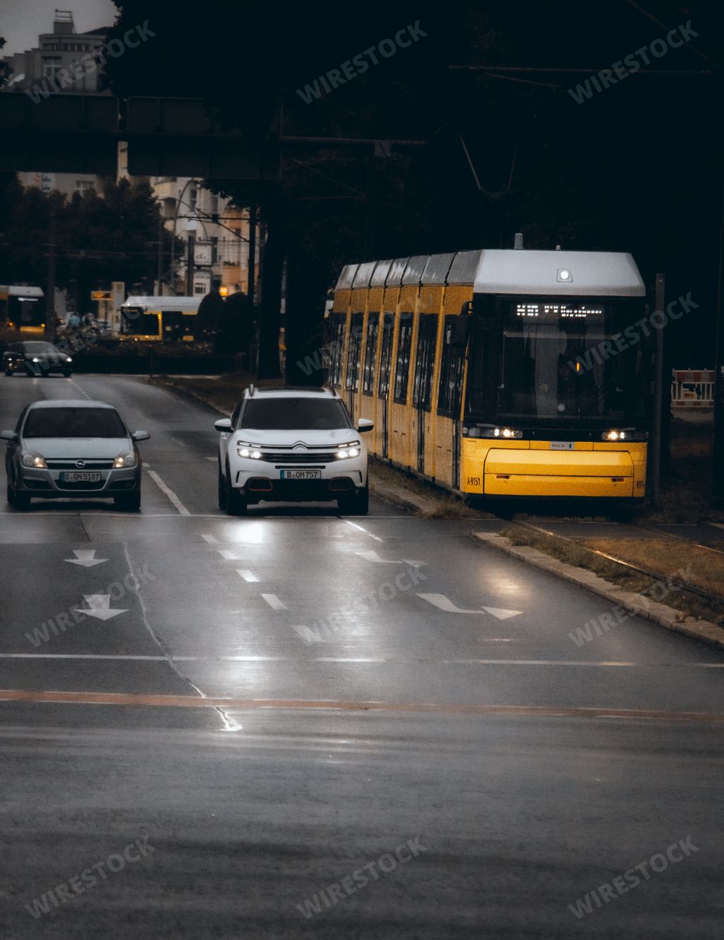 White cars and yellow city tram, on a road on a street in Berlin, Germany, with lights turned on