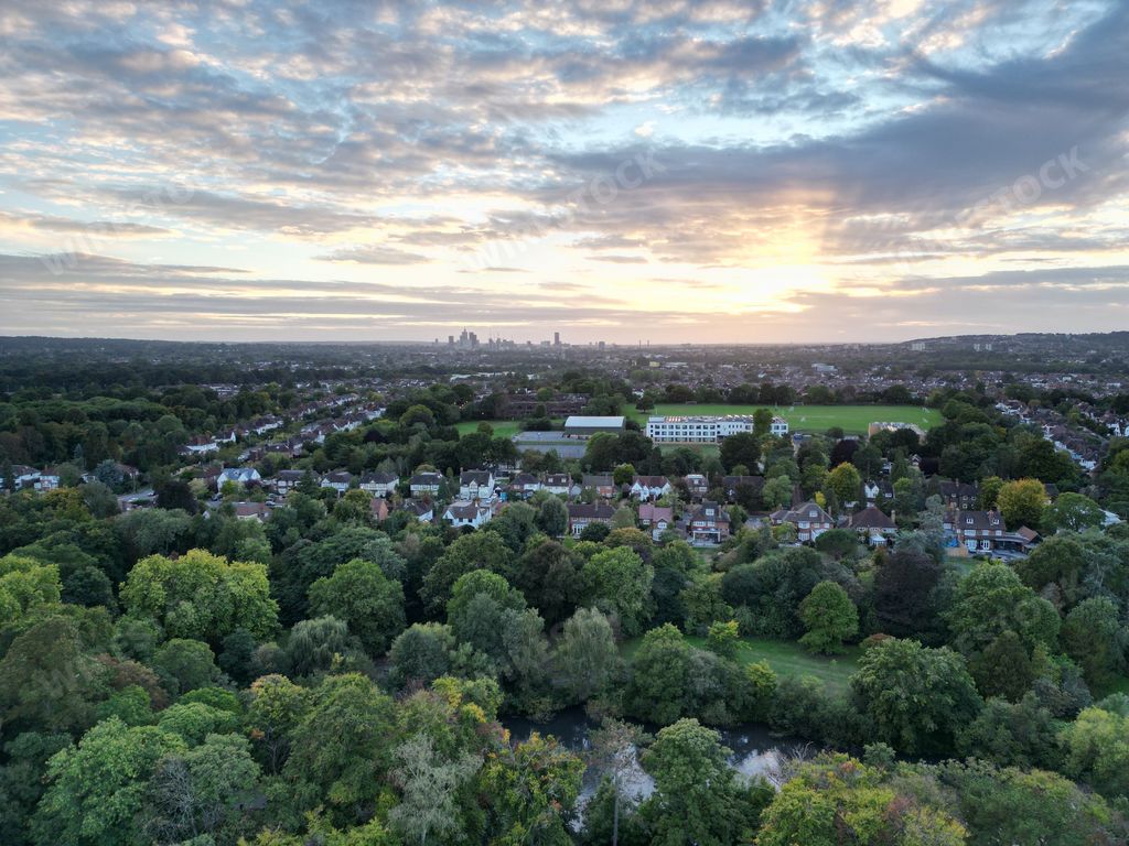 A high-angle shot of a city full of buildings, green trees, fields and roads at Bromley borough.