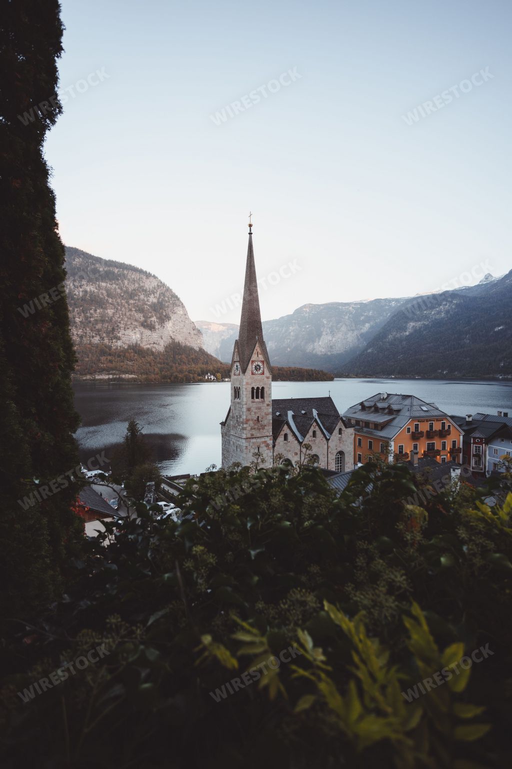 A vertical shot of the Hallstatt Lutheran Church with trees and a lake in the background