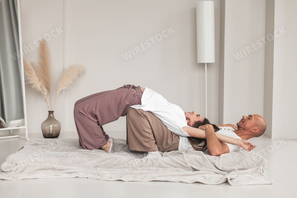 A middle-aged Caucasian bald masseur and a woman doing Japanese massage exercises on a mat at home