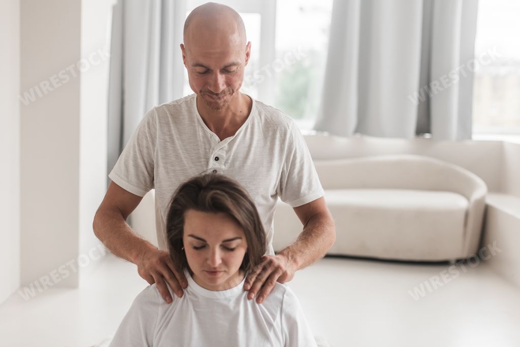 A middle-aged Caucasian bald masseur and a woman doing Japanese massage exercises on a mat at home