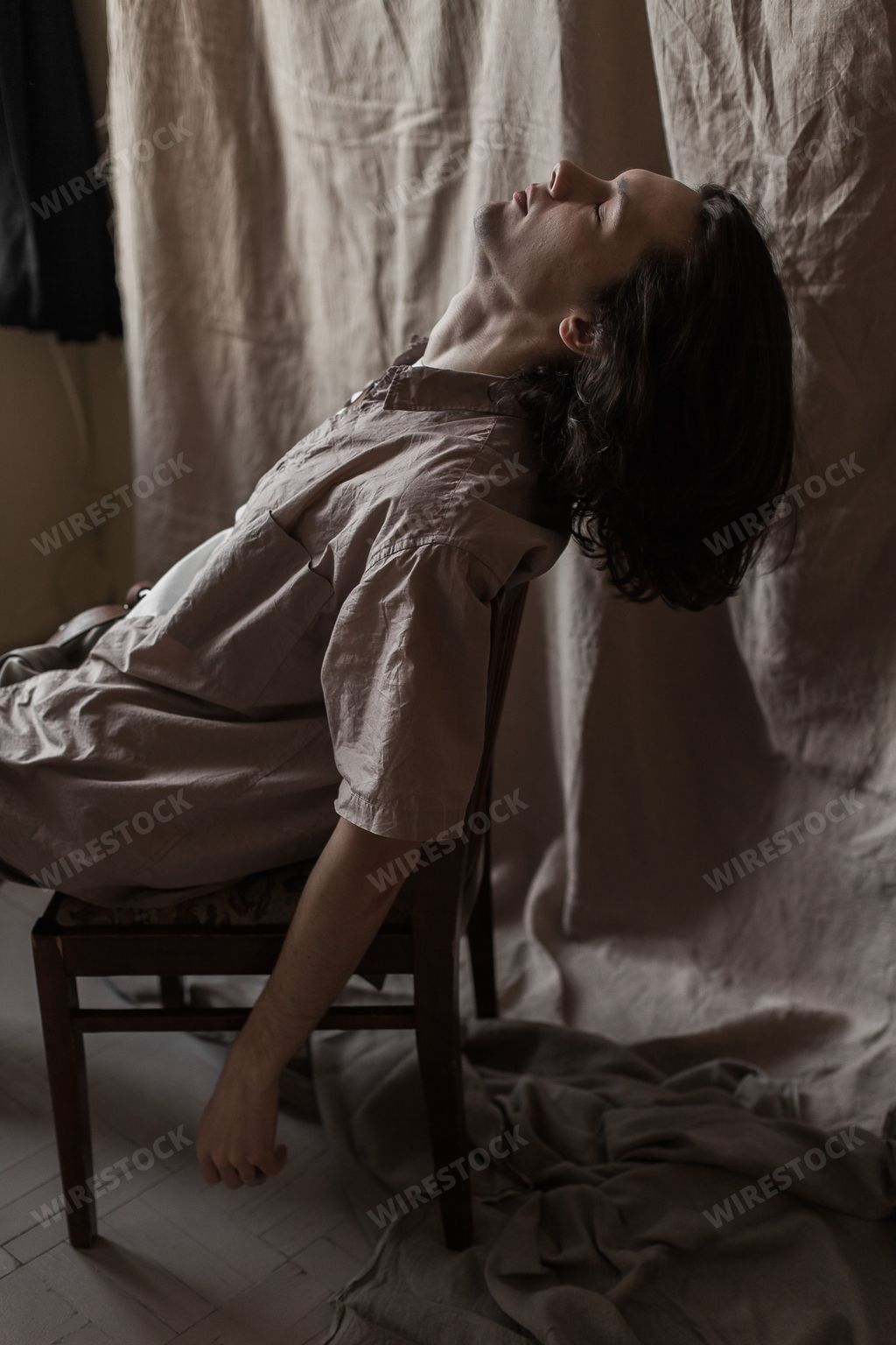 An aesthetic vertical shot of a handsome young man in silk clothing against a beige background