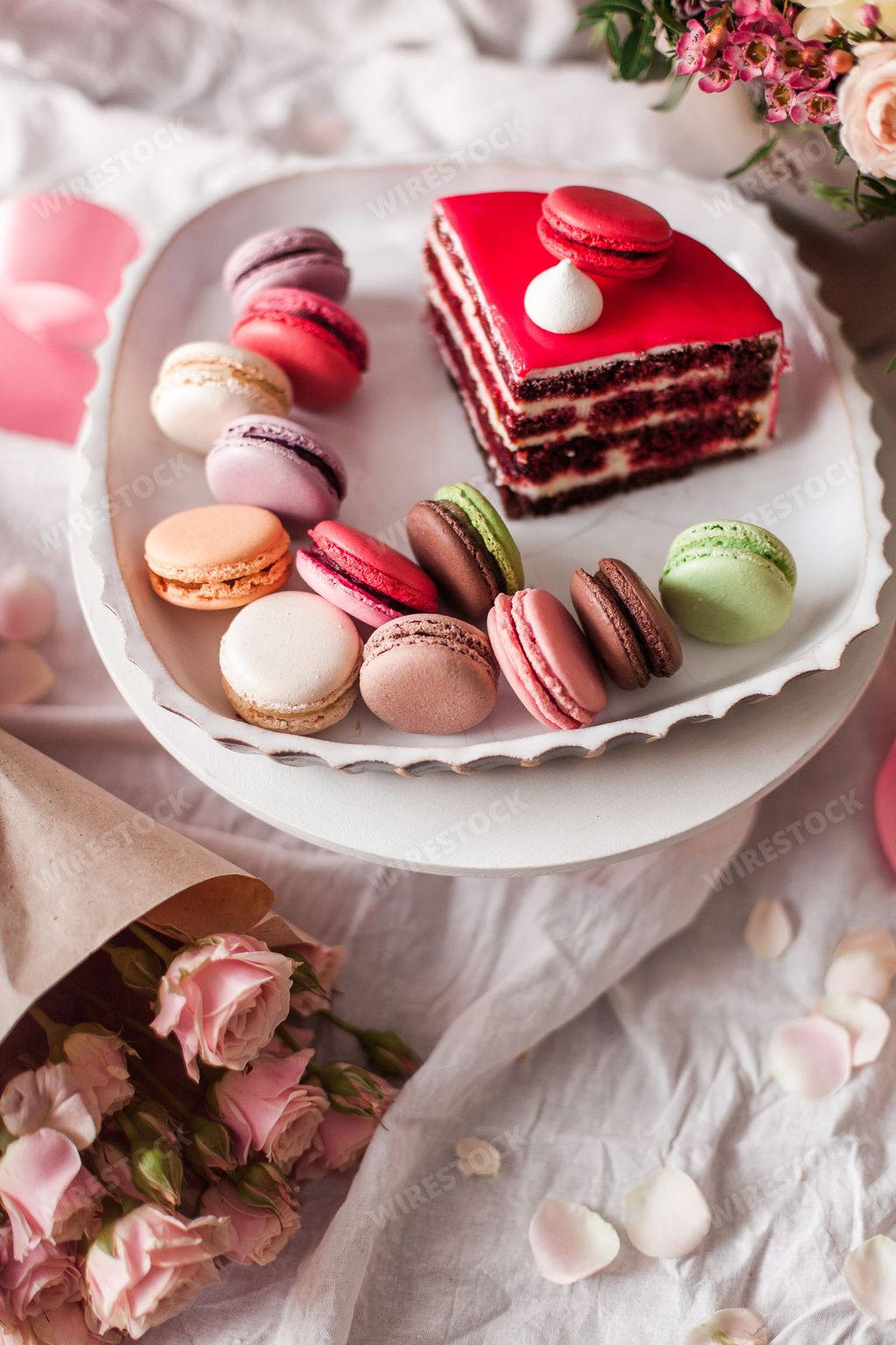 An aesthetic shot of colorful macarons and a cake piece arranged with flowers