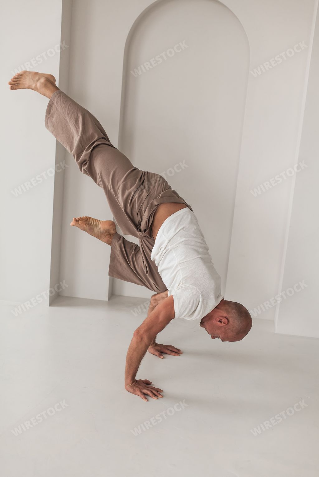 An athletic bald Russian male practicing yoga in a white studio. Healthy lifestyle concept.