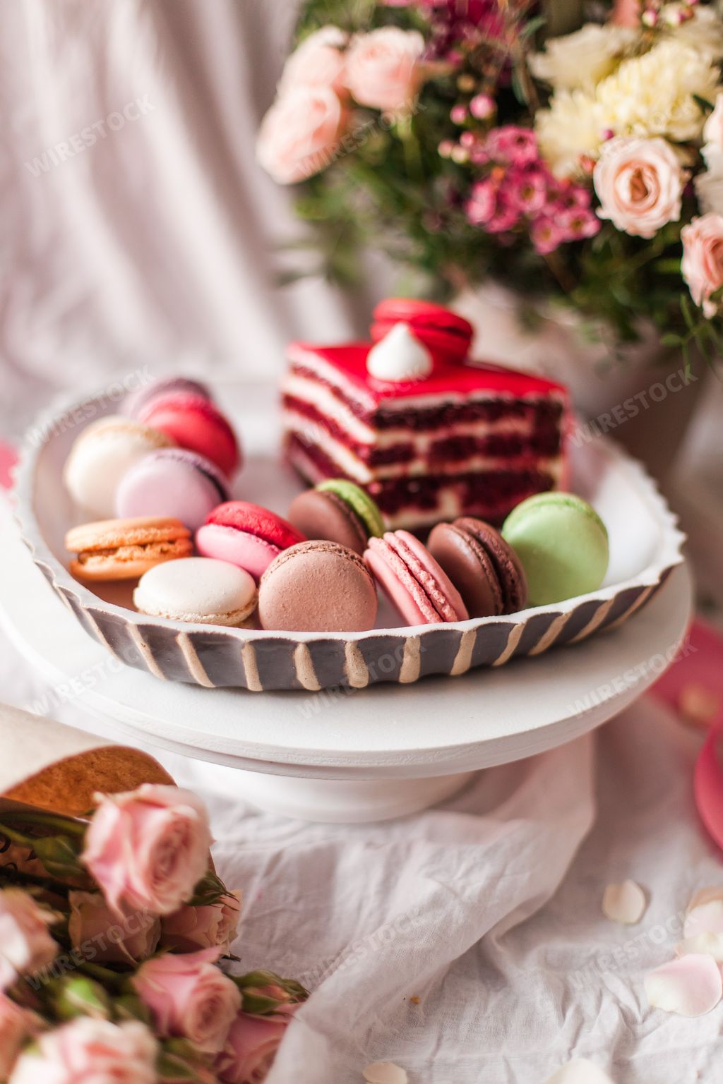 An aesthetic shot of colorful macarons and a cake piece arranged with flowers