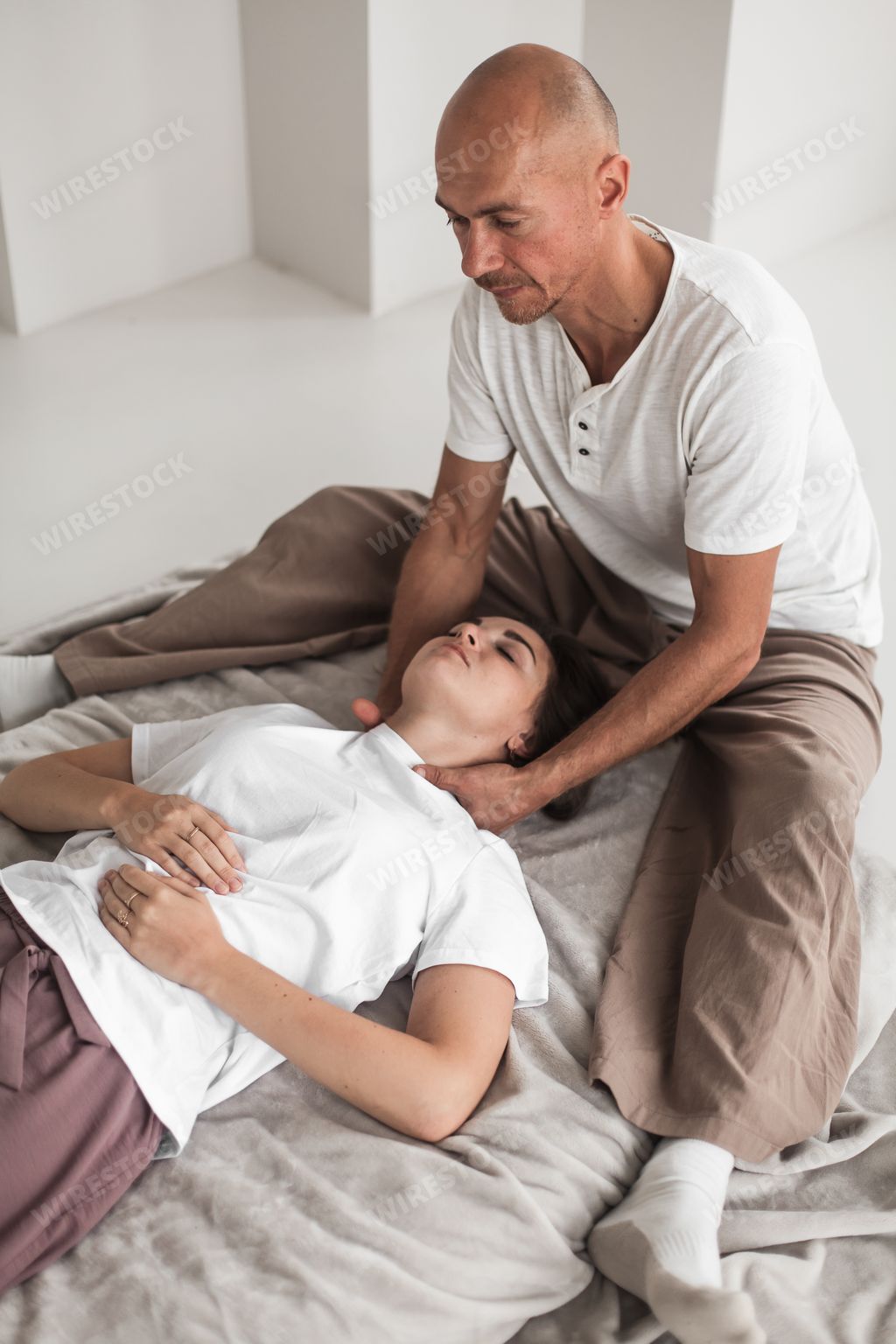 A professional young man massaging a woman's neck in a white cozy room during a manual therapy