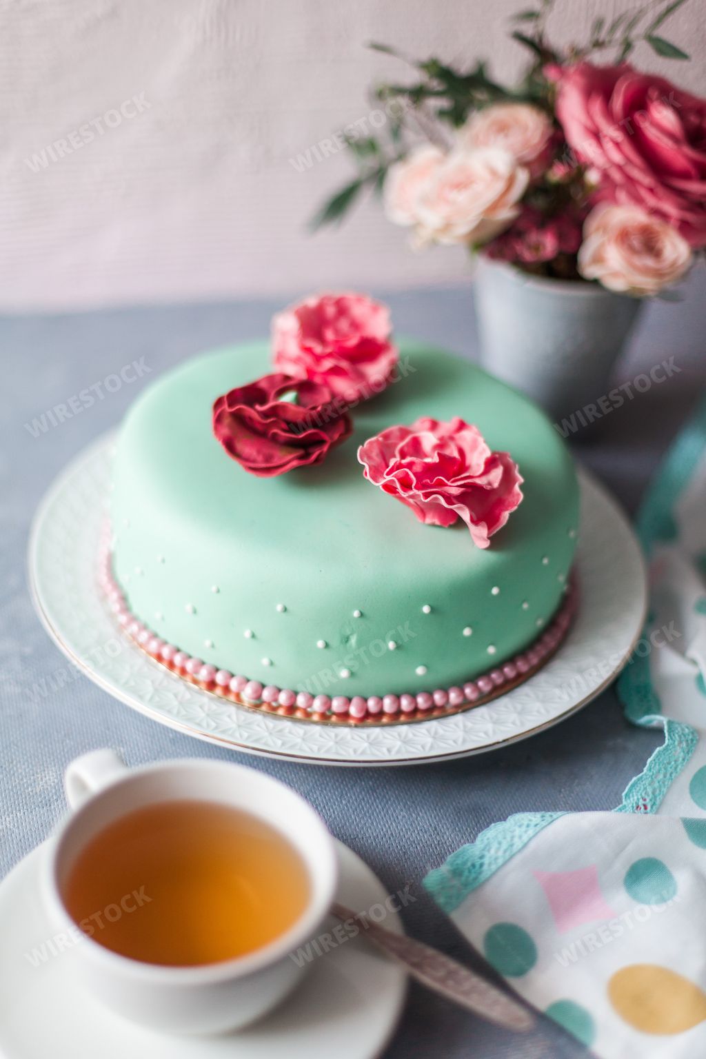 An aesthetic shot of a cake covered by turquoise marzipan and arranged with flowers