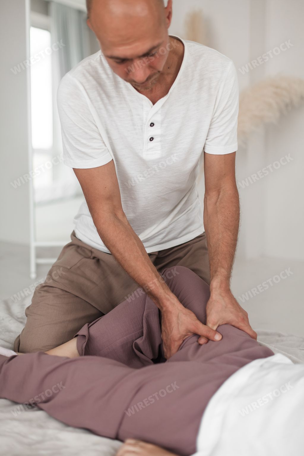 A middle-aged Caucasian bald masseur and a woman doing Japanese massage exercises on a mat at home