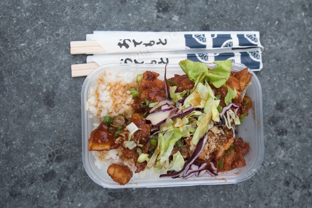 A top view of a Korean chicken meal in a plastic container with chopsticks