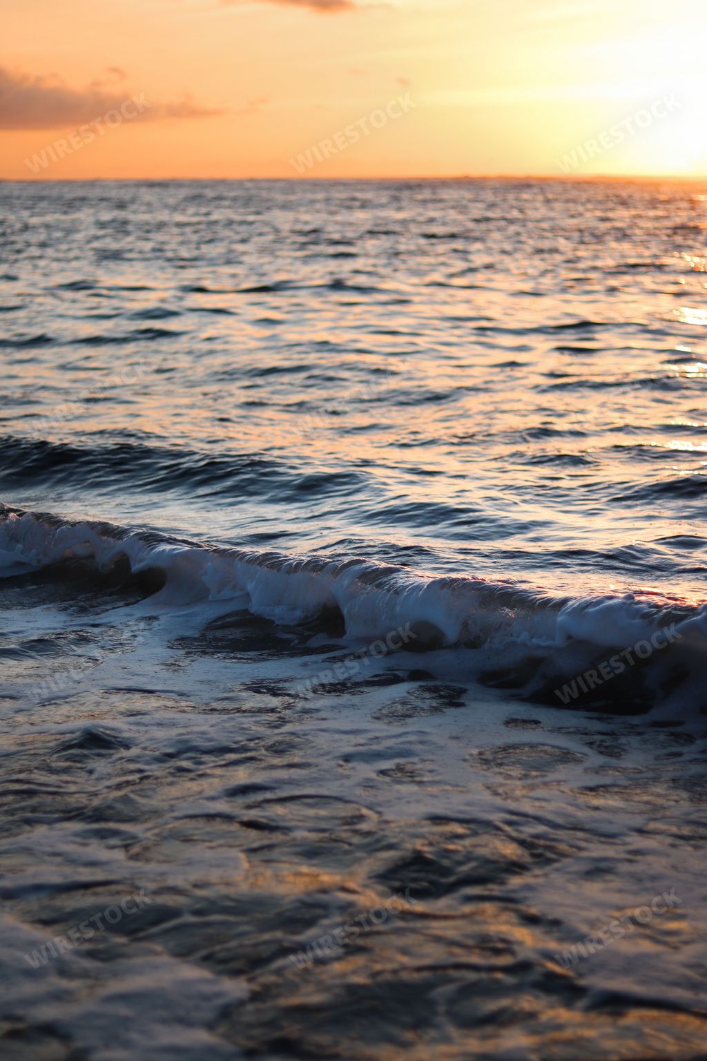 A vertical shot of sea waves covering the coastline in the sunset