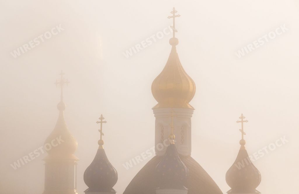 The bell towers and domes of an Orthodox church covered with dense fog in the morning